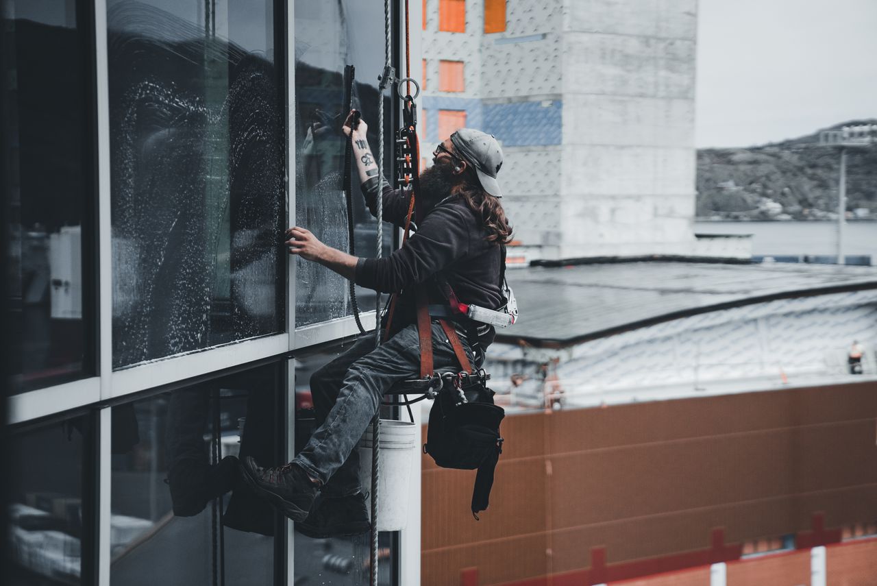 services-01 A man cleaning skyscraper windows with a harness, showcasing urban high-rise work.